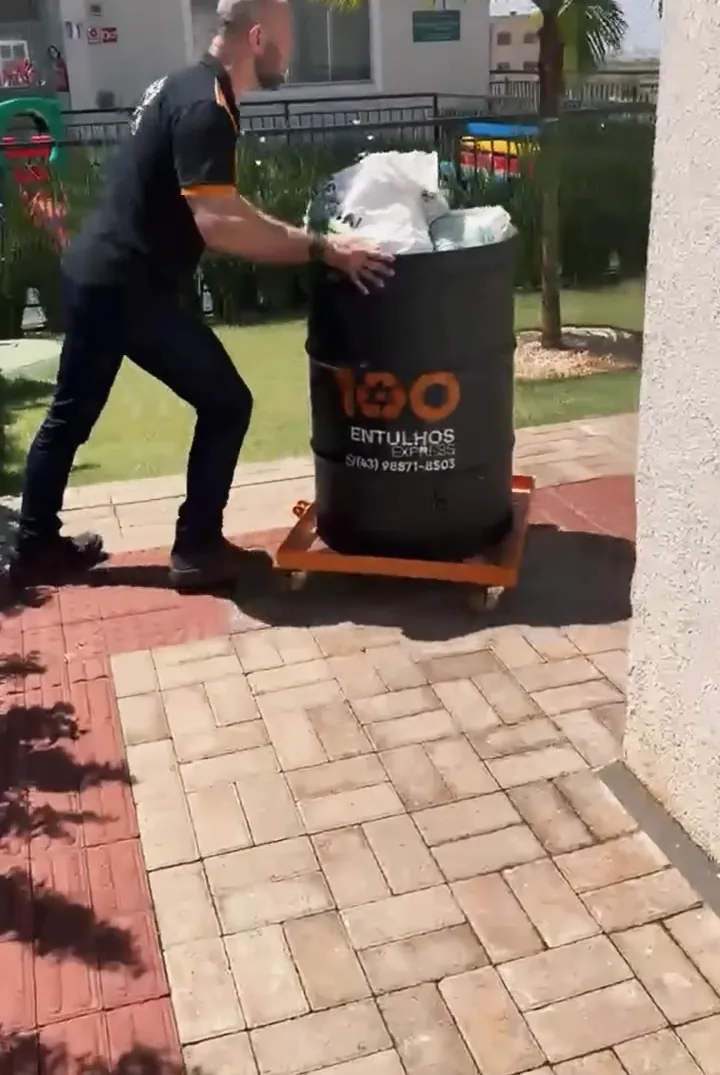 Funcionário levando o coletor pela calçada de um condomínio